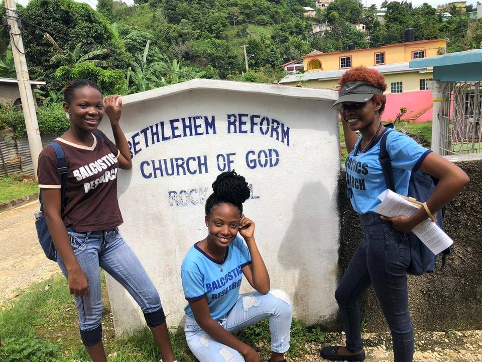 Three Balcostics Research interviewers beside the Bethlehem Reform Church of God sign during household fieldwork
