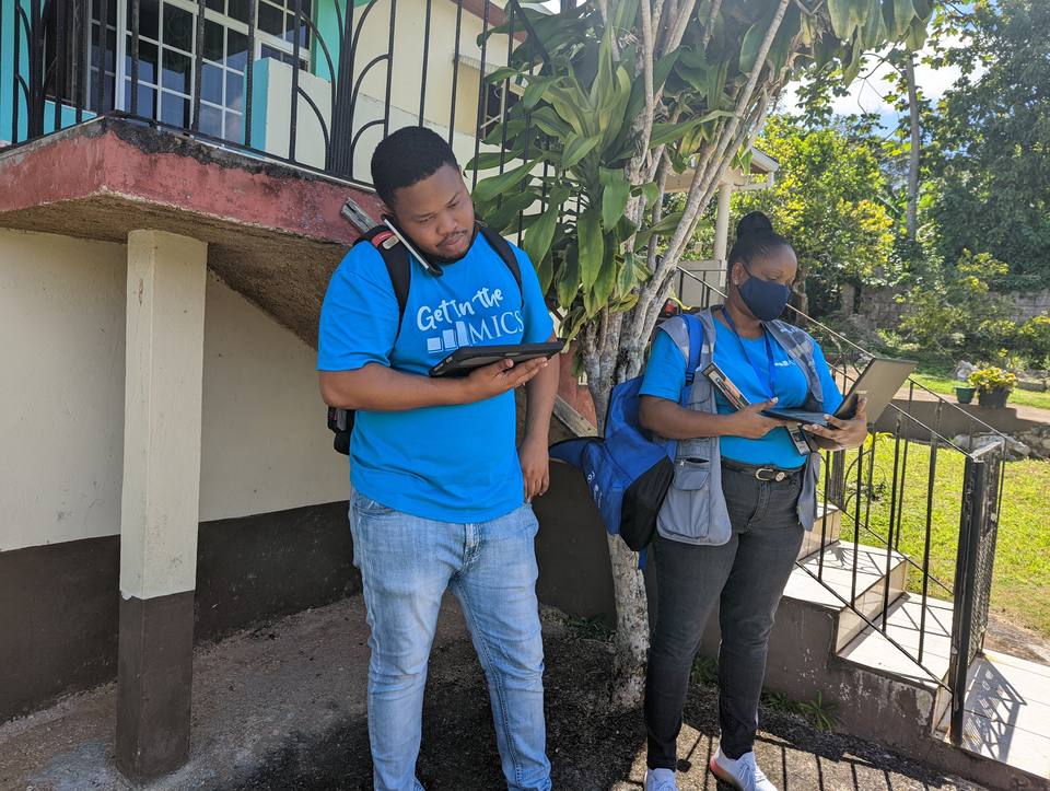 Two MICS interviewers in blue field shirts checking tablets before a household visit